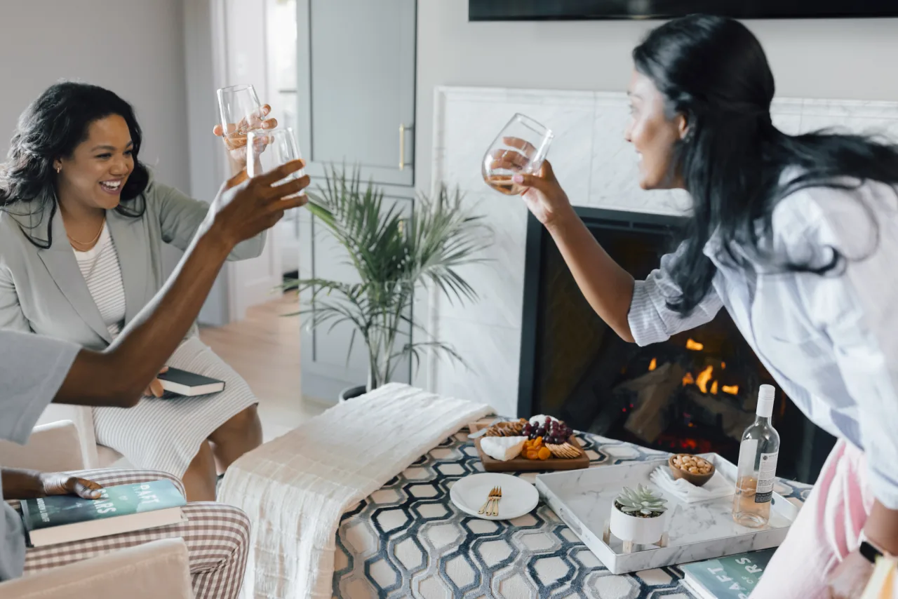 Two friends toasting with wine beside a modern fireplace in a bright, welcoming living room
